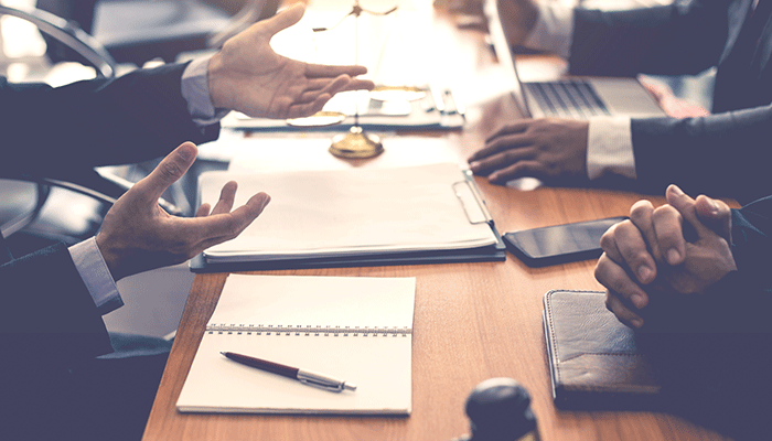 Grupo de personas reunidas, donde una persona da una explicación y mueve sus manos 